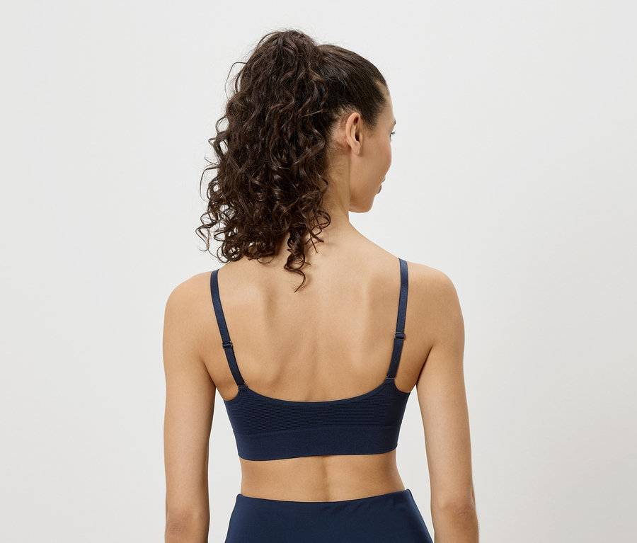 Rückansicht einer Frau mit lockigem Haar, die einen marineblauen Sport-BH trägt.