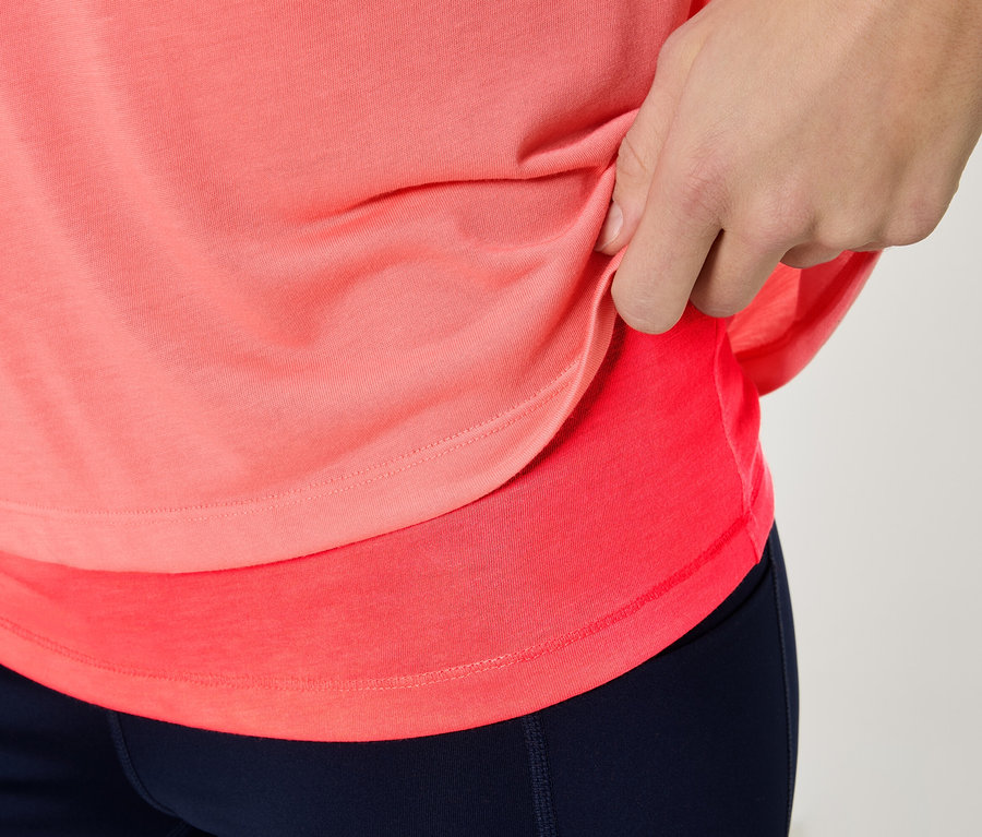 Nahaufnahme einer Person, die ein korallfarbenes Sportoberteil und marineblaue Leggings trägt.