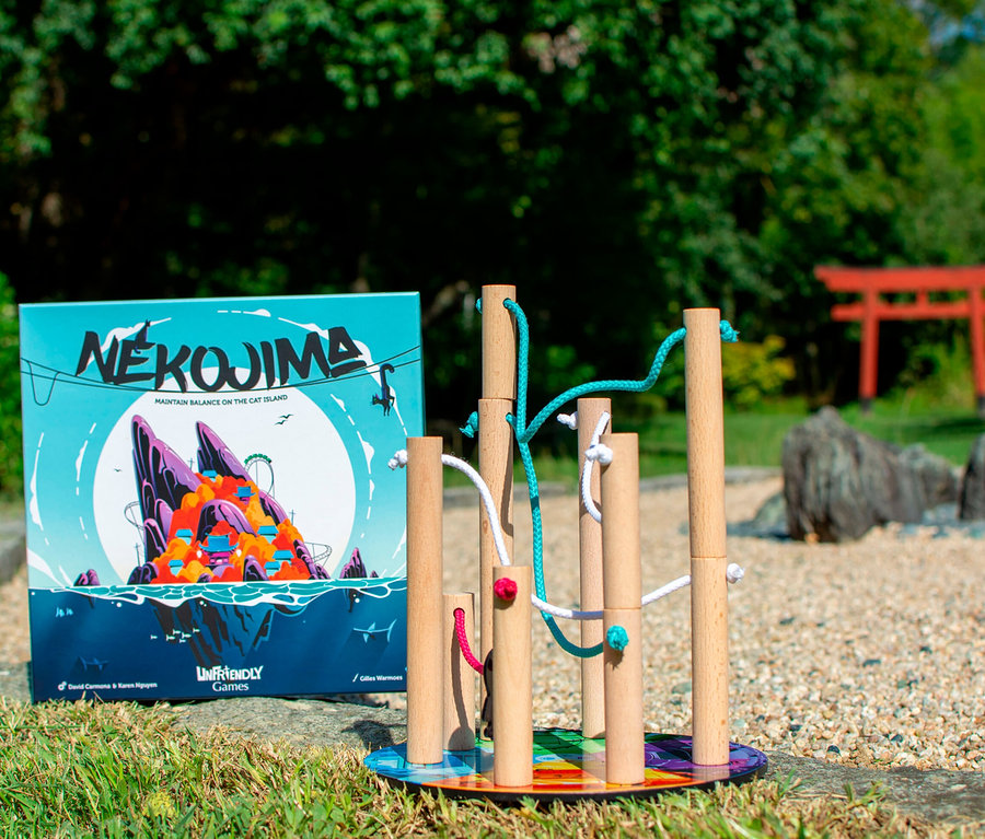 Das Spiel »Nekojima« steht neben einem Holzspielzeug mit bunten Schnüren auf einem Rasen.