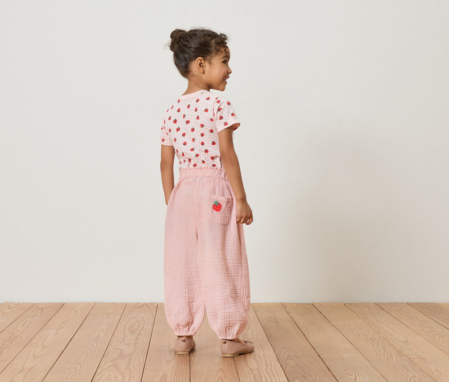 Mädchen von hinten, trägt Erdbeer-T-Shirt und rosafarbene Hose mit Erdbeer-Detail.