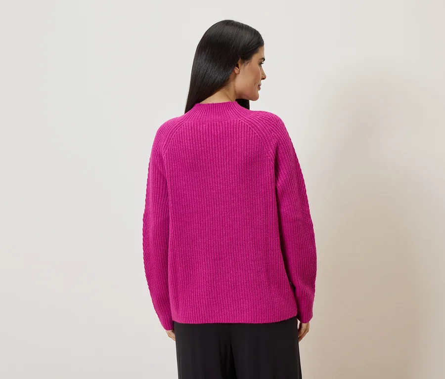Rückansicht einer Frau mit langen, dunklen Haaren, die einen pinkfarbenen Strickpullover und eine schwarze Hose trägt.