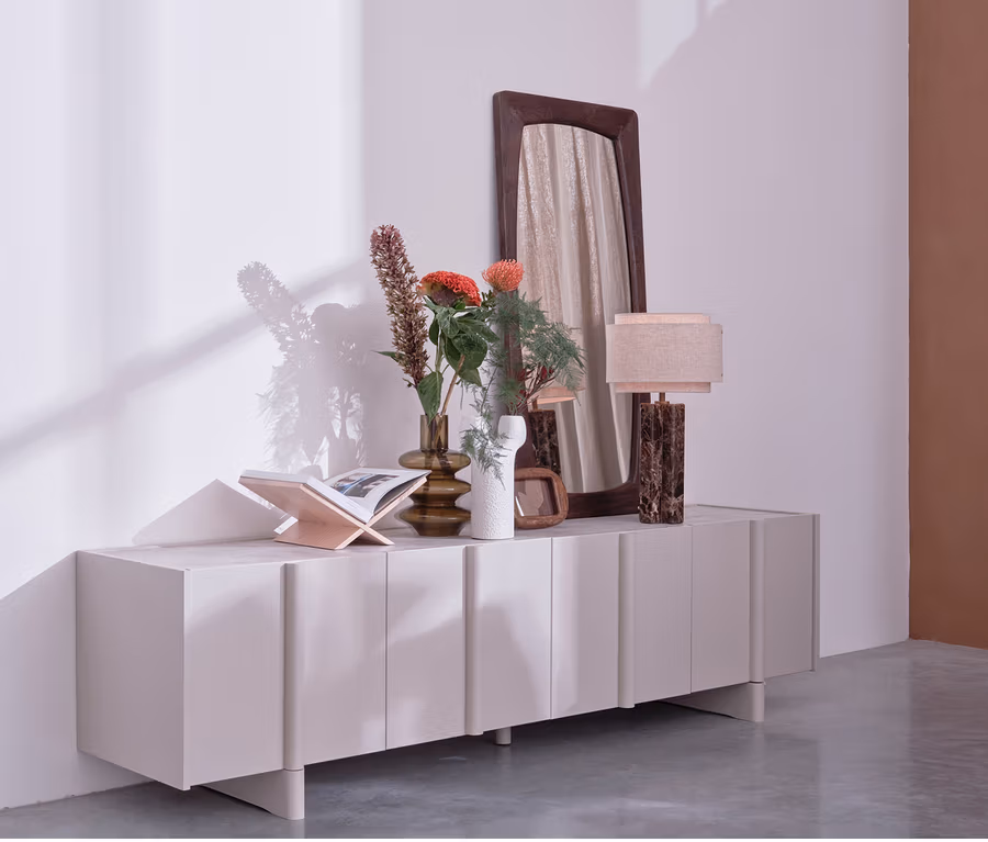 Auf einem WOOOD Lowboard »Basu« kiefer dust stehen Vasen mit Blumen, ein Buch, eine Lampe und ein Spiegel.