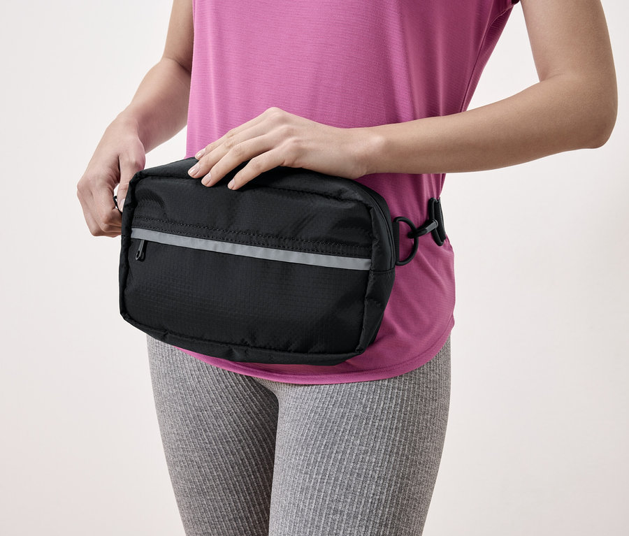 Eine Frau mit einer schwarzen Hüfttasche mit reflektierendem Streifen.