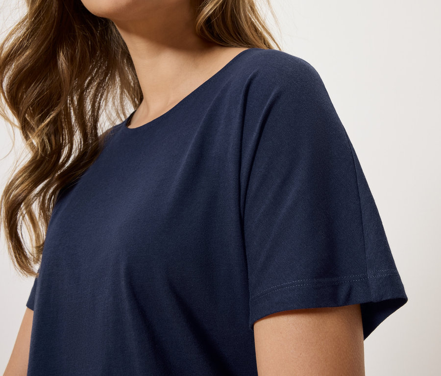 Nahaufnahme einer Frau mit gewelltem, braunem Haar, die ein marineblaues T-Shirt trägt.