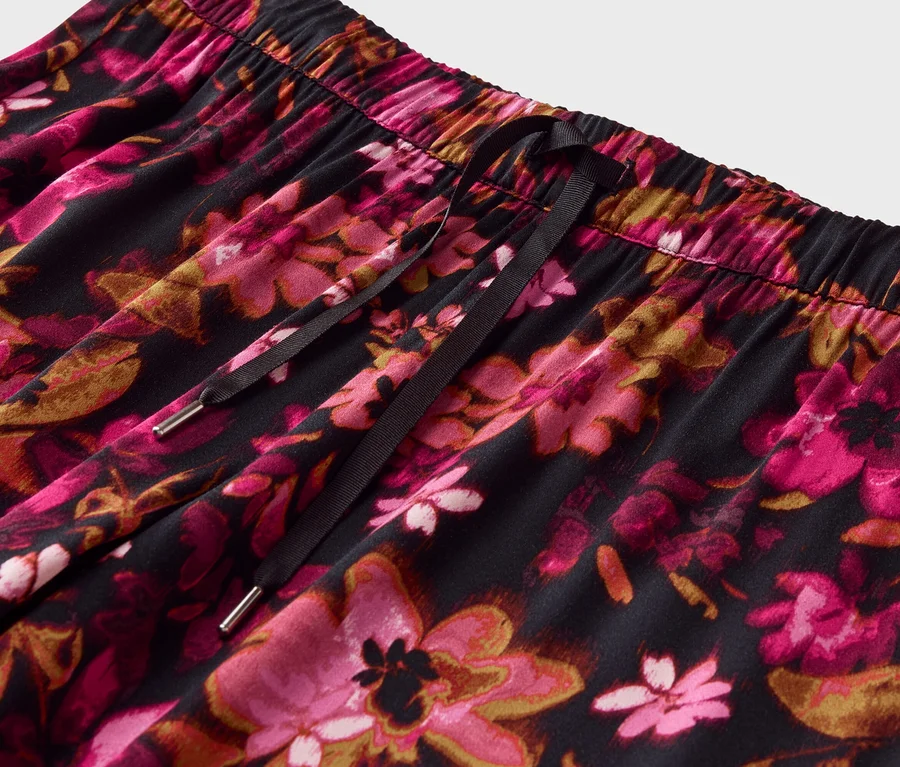 Nahaufnahme einer Hose mit Gummizug und Kordel, bedeckt mit einem pinkfarbenen Blumenmuster auf schwarzem Grund.