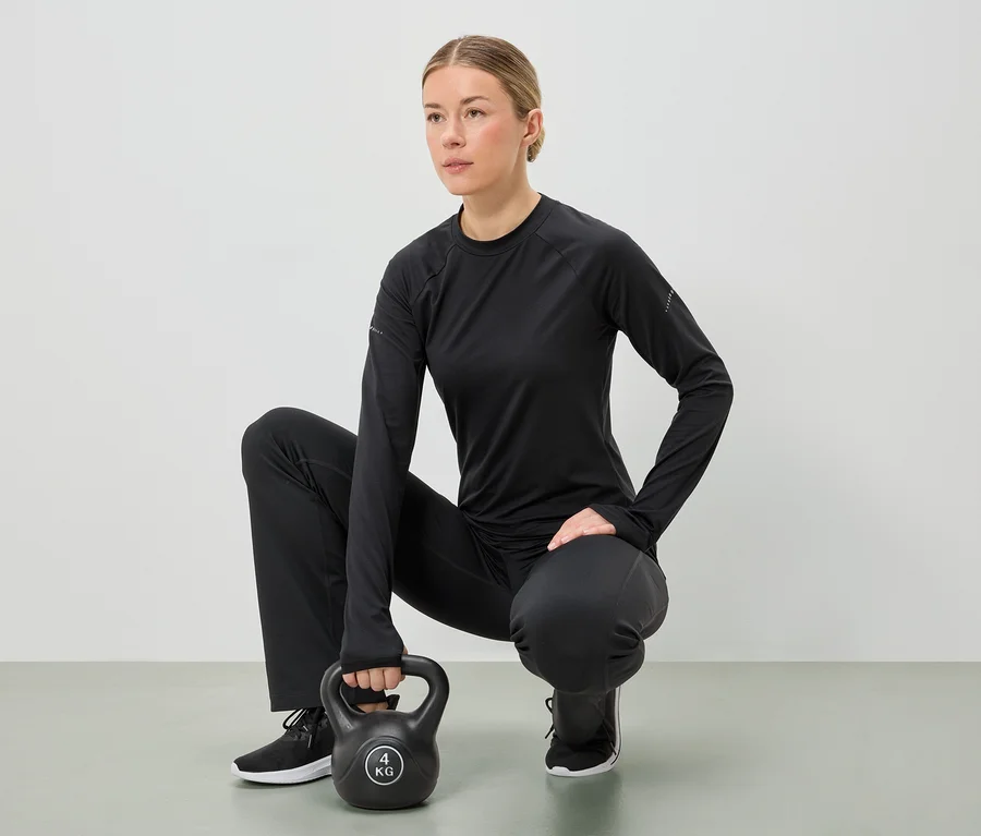 Eine Frau in schwarzer Sportbekleidung hockt und hält eine 4-kg-Kettlebell mit beiden Händen.