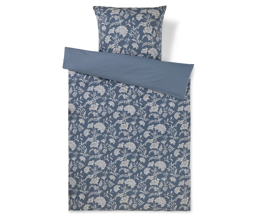 Ein blaues Bettwäsche-Set mit weißem Blumenmuster. Der obere Teil des Bettbezugs ist umgeschlagen und zeigt eine einfarbige blaue Unterseite.