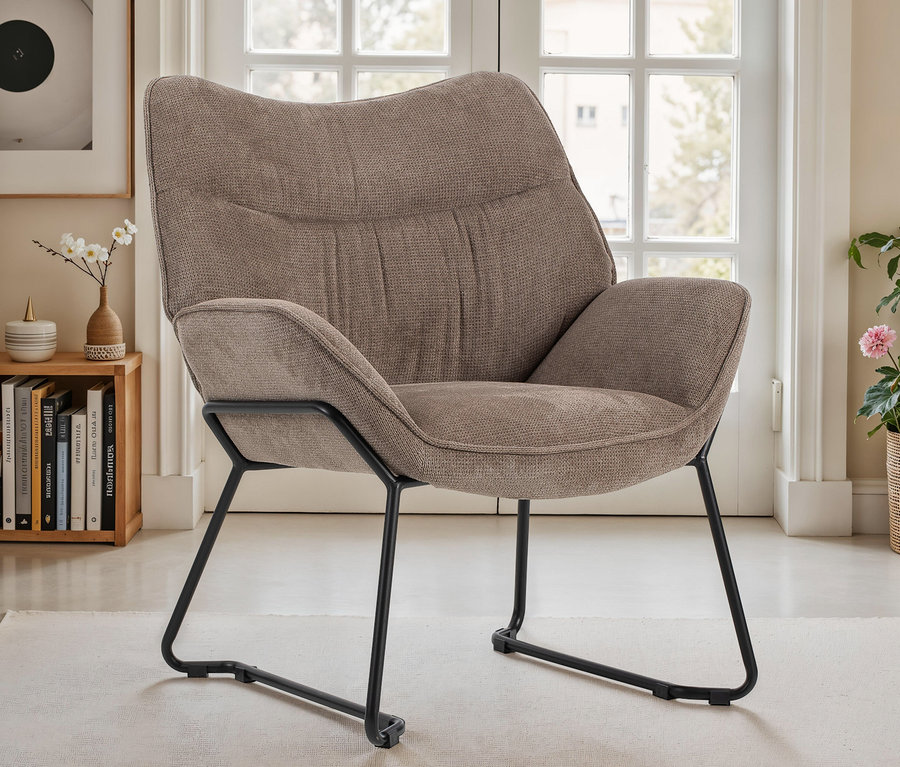 Brauner DeVries Sessel »Aliano« mit schwarzem Metallgestell auf einem hellen Teppich vor einer Fenstertür.