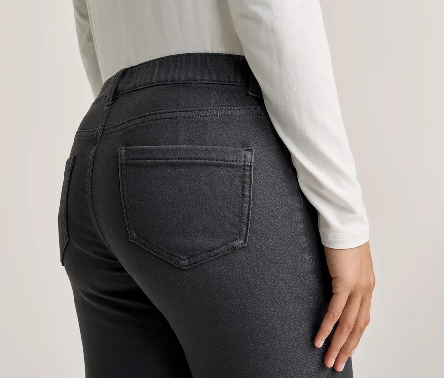 Rückenansicht einer Person, die eine weiße Langarmbluse und eine dunkle, graue Hose mit Gesäßtaschen trägt.