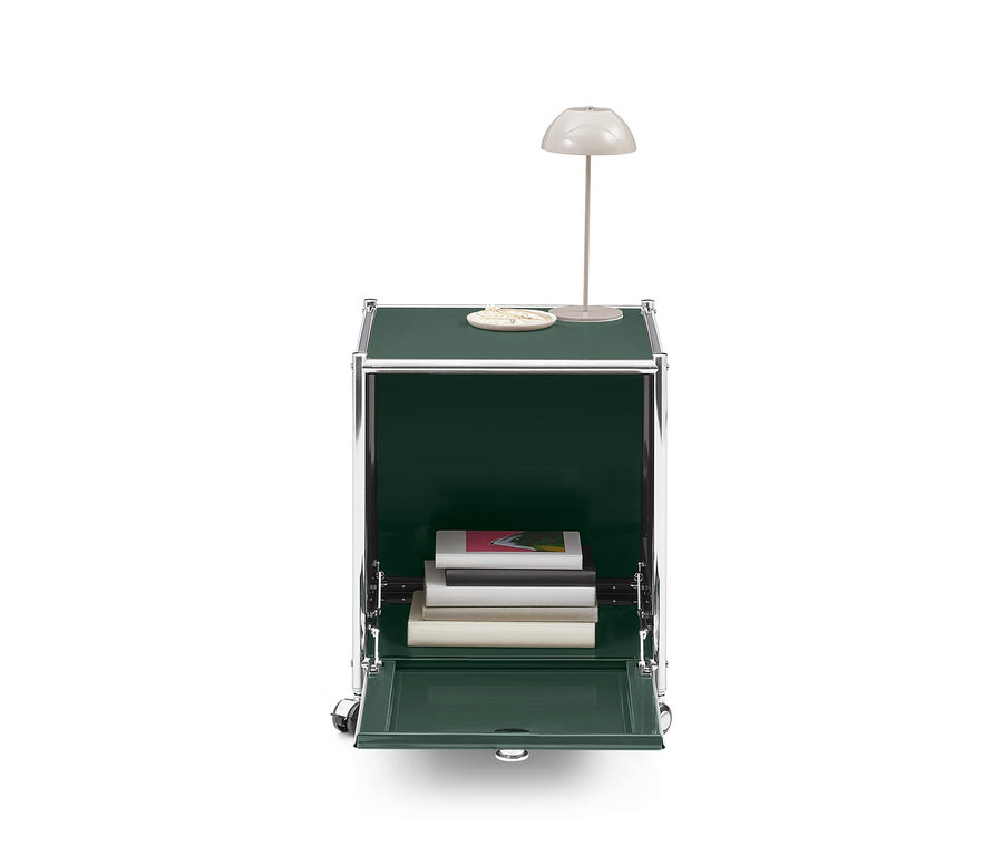 Dunkelgrüner Rollcontainer mit Chromrahmen, offener Klapptür, Büchern innen, einer Tischlampe und einem Dekoobjekt oben.