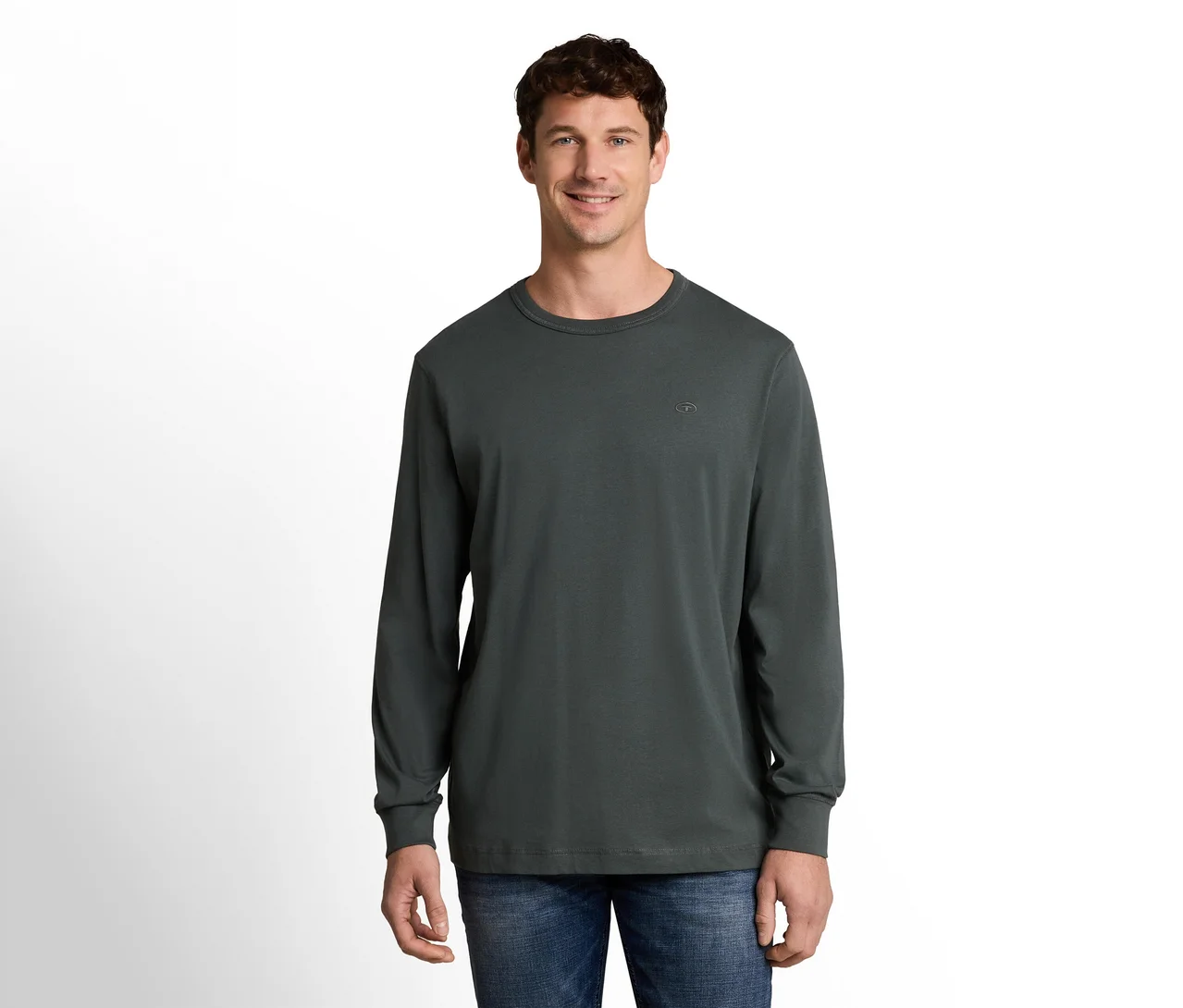 Ein lächelnder Mann mit kurzen braunen Haaren steht frontal, trägt ein dunkelgraues Langarmshirt und blaue Jeans vor weißem Hintergrund.