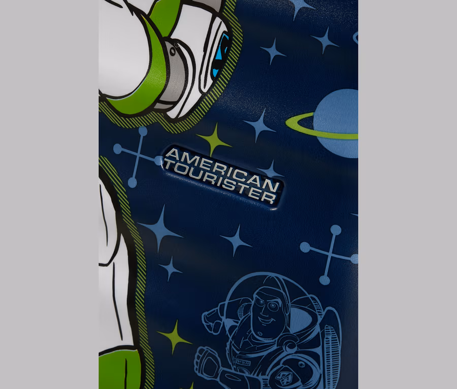 Nahaufnahme eines dunkelblauen Koffers mit Weltraum-Motiv. Er zeigt ein silbernes „AMERICAN TOURISTER“-Logo, eine große Grafik von Buzz Lightyears Kopf und Schulter links und eine kleinere Umrisszeichnung von Buzz Lightyear rechts unten, umgeben von Sternen, Planeten und geometrischen Symbolen.