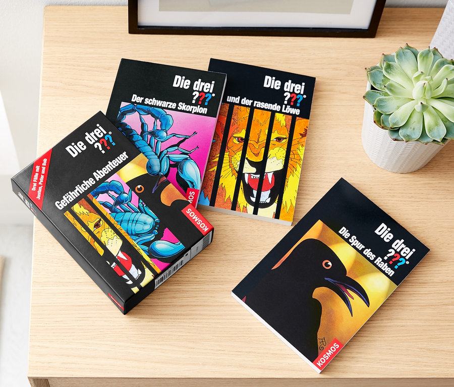 Vier »Die drei ???« Taschenbücher liegen nebeneinander auf einem Tisch. Die Cover zeigen gefährliche Abenteuer, einen schwarzen Skorpion, einen rasenden Löwen und die Spur des Raben.