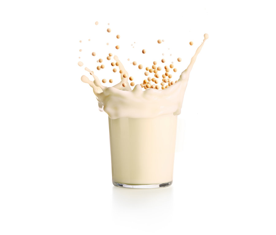 Milch spritzt aus einem Glas, umgeben von kleinen Kugeln. Lékué Nuss- und Getreidemilch-Maker.