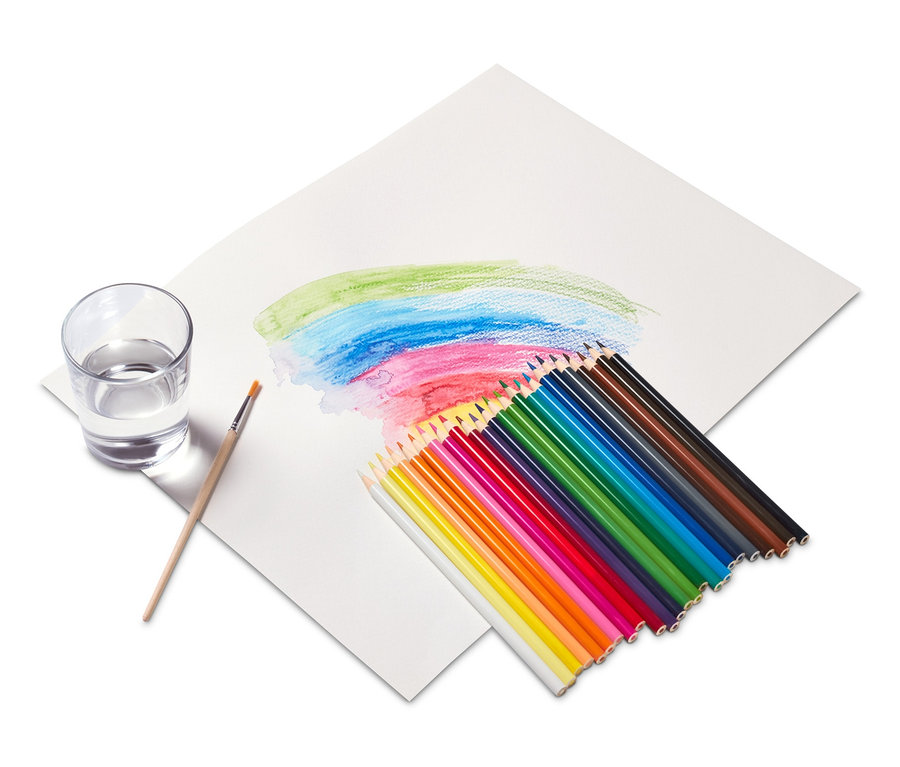 Aquarell-Buntstifte und ein Pinsel liegen auf Papier neben einem Glas Wasser.
