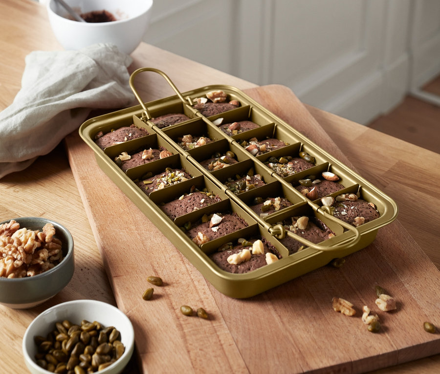 Eine goldene Brownie-Backform mit Griff, gefüllt mit kleinen Brownies auf einem Schneidebrett.