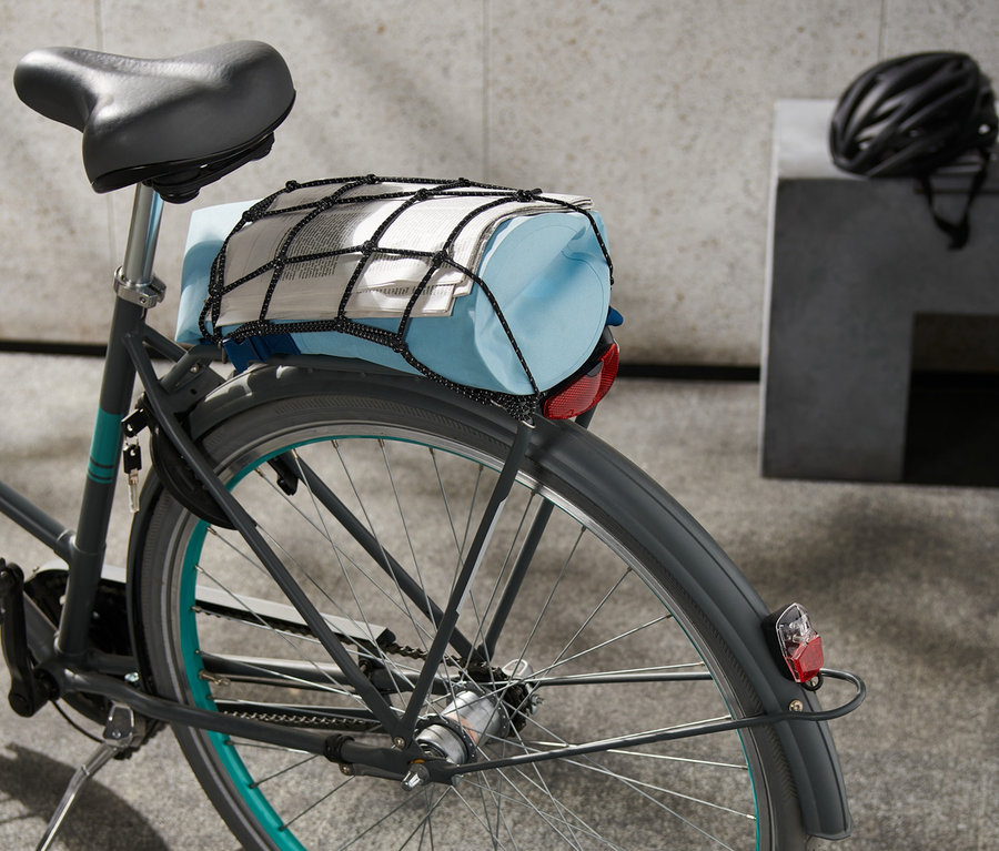 Auf einem Fahrrad befindet sich ein Fahrrad-Gepäcknetz, das eine blaue Tasche und eine Zeitung hält.