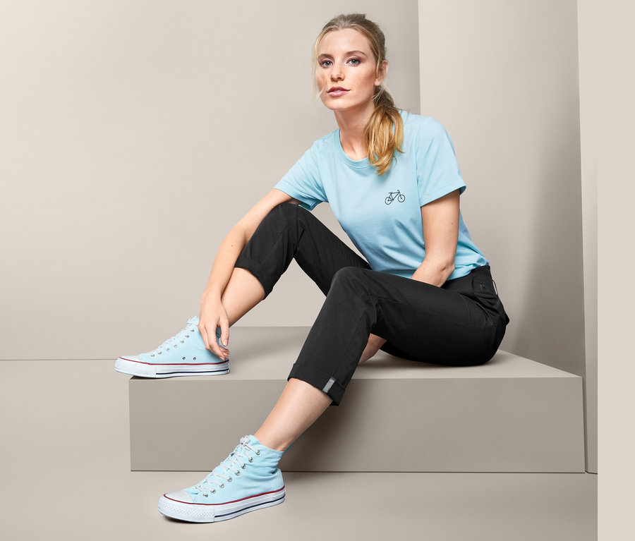 Eine Frau sitzt auf einer Treppe und trägt eine Funktionshose, ein blaues T-Shirt und blaue Turnschuhe.
