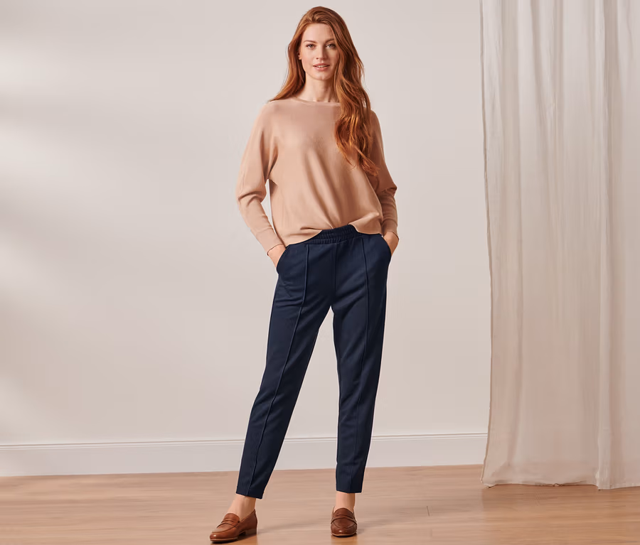 Frau posiert in beigem Pullover und dunkelblauer Joggpants mit Biese.