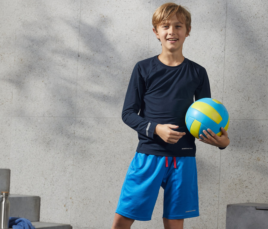 Ein Junge hält einen Volleyball und trägt ein Funktionsshirt aus recyceltem Material.