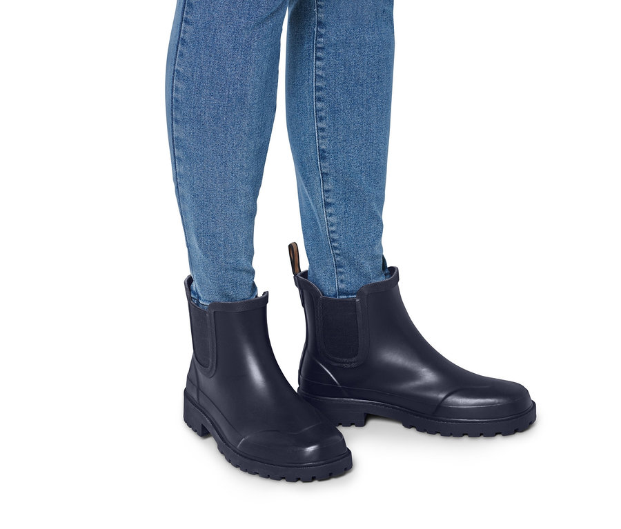 Beine in Jeans und Regenstiefeletten.