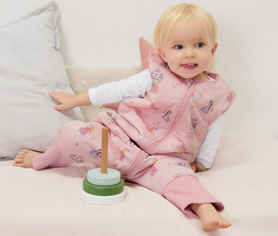Kleinkind sitzt auf Matratze und trägt einen Schlafsack mit Beinen, 2,5 TOG, ca. 90 cm.