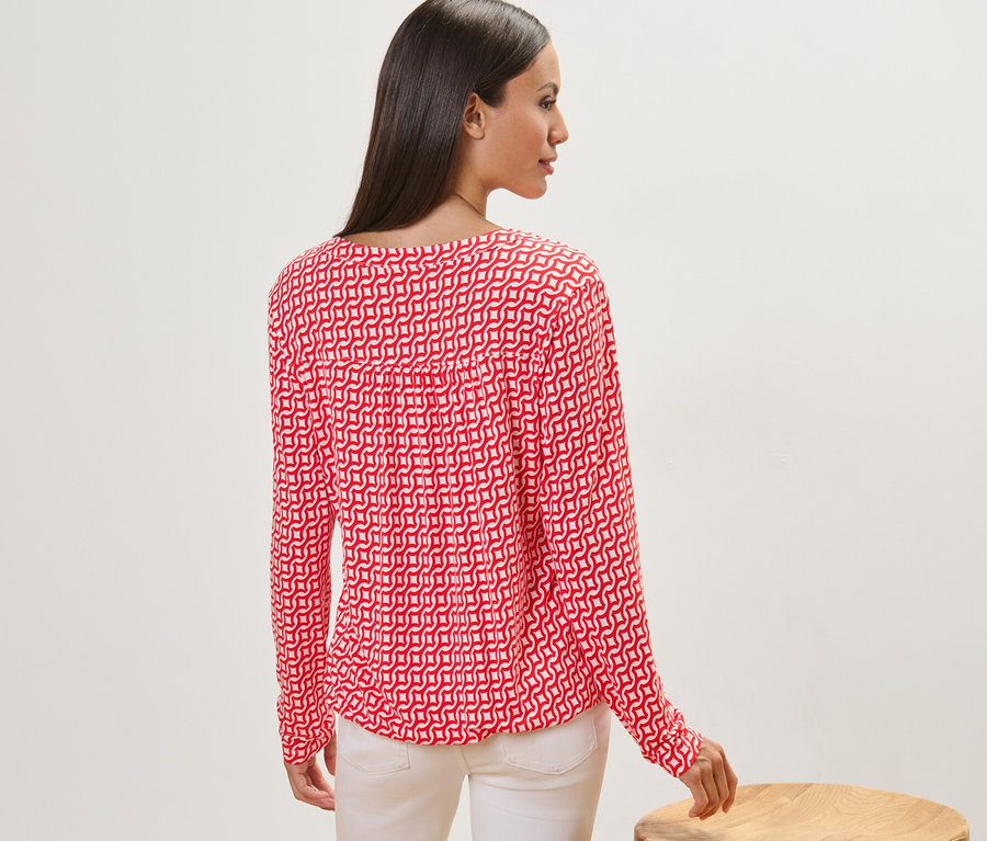 Frau steht mit dem Rücken zur Kamera und trägt ein bedrucktes Blusenshirt, rot.