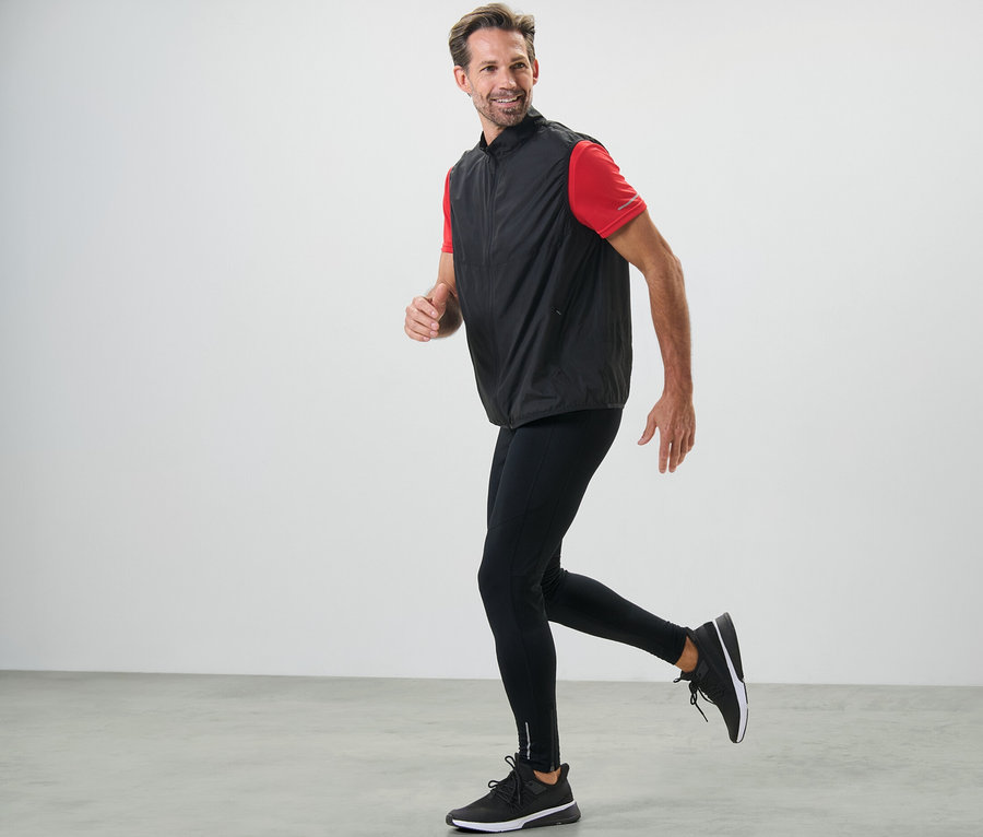 Mann in schwarzen Lauftights und Weste läuft.