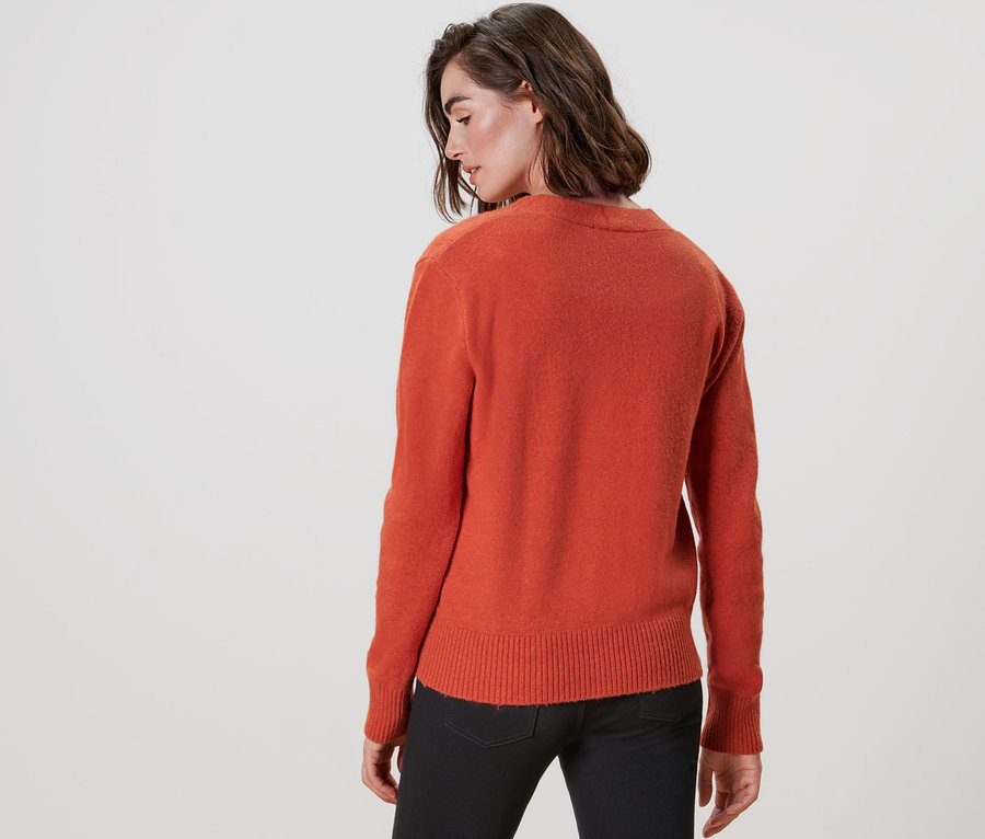 Rückansicht einer Frau, die einen orangefarbenen Cardigan mit V-Ausschnitt und eine schwarze Hose trägt.