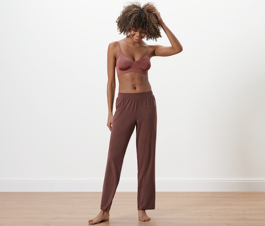 Frau mit Afro steht barfuß und trägt eine Pyjamahose und ein Bralette.