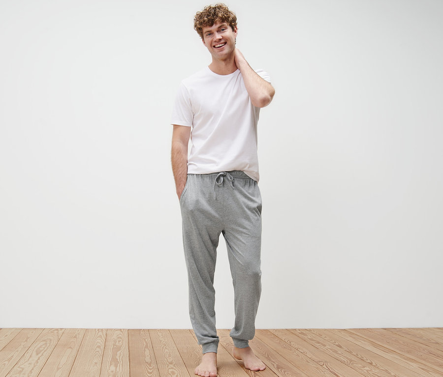 Mann steht mit Händen in den Taschen der grauen 2 Pyjamahosen.