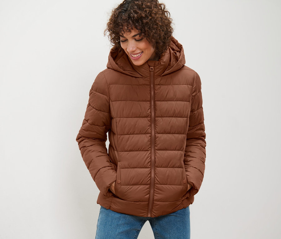 Frau trägt eine cognacfarbene Steppjacke mit Kapuze und blickt nach unten.