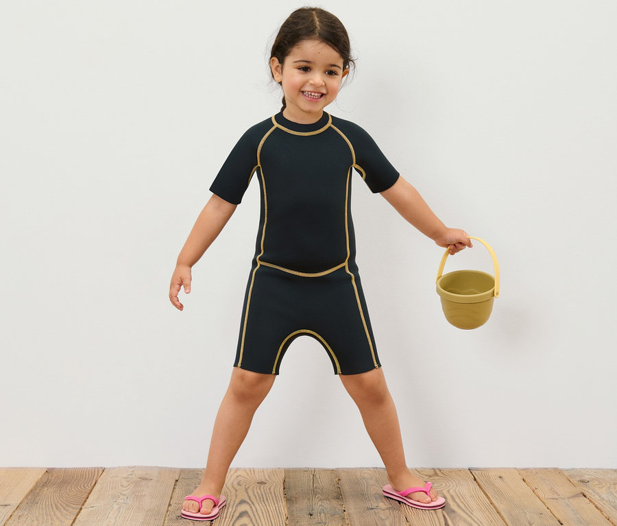 Mädchen im Kinder-Neoprenanzug hält gelben Eimer.