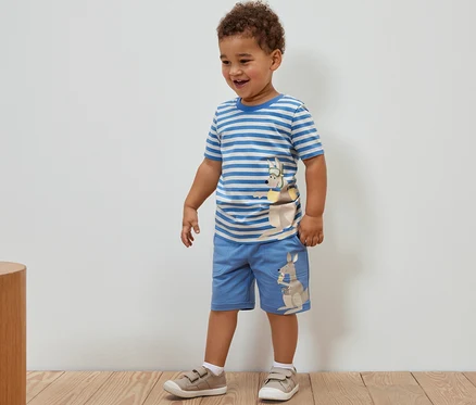 Ein Junge steht und trägt ein 2 Kinder-T-Shirts mit Applikation und Shorts mit Känguru-Applikation.
