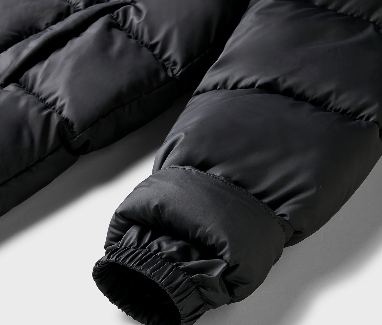 Detailaufnahme eines schwarzen Steppmantelärmels mit elastischem Bündchen.