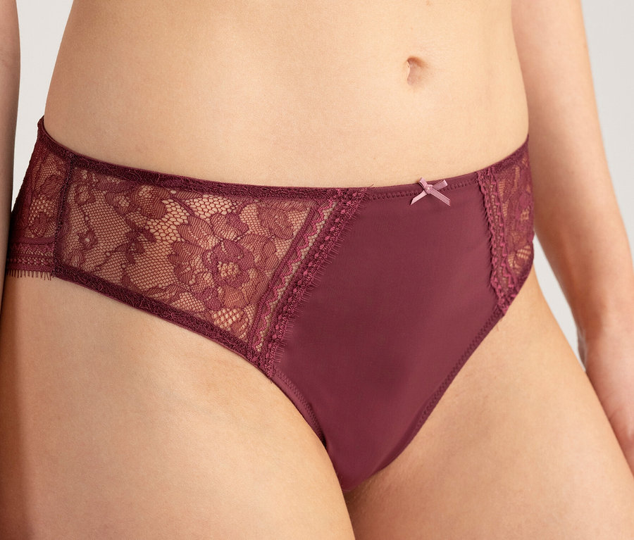 Oberkörper einer Person, die einen Passionata Highwaist Slip »Jeanne« in Bordeauxrot mit Spitzenbesatz an den Seiten und einer kleinen Schleife trägt.