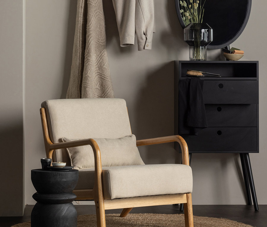 Beiger Sessel neben schwarzem Woood Hocker »Bikkel« auf Jute-Teppich.