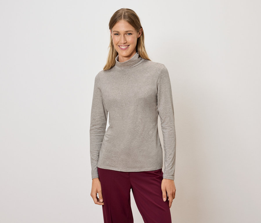 Frau posiert in einem grauen Rollkragenpullover und weinroten Hosen.