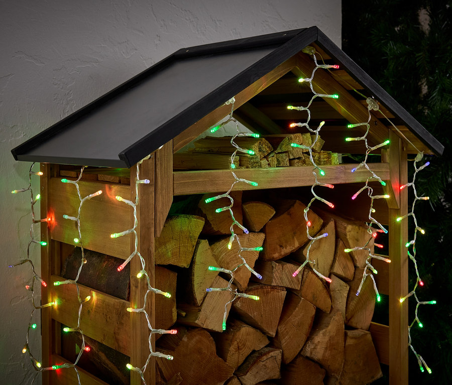 Holzschuppen gefüllt mit Holzscheiten, dekoriert mit bunten Lichtern.