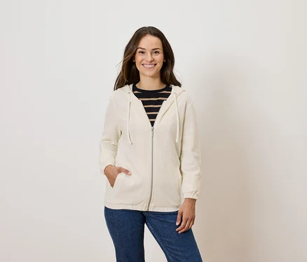 Frau posiert in cremefarbener Zip-Hoodie und blauen Jeans.