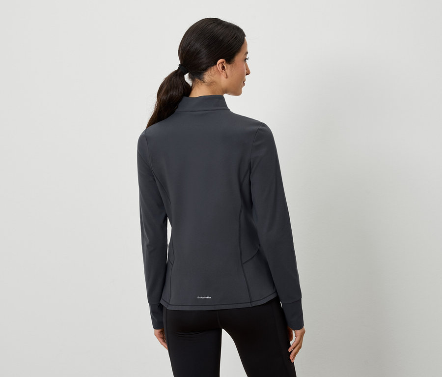 Frau mit braunen, zu einem Pferdeschwanz zusammengebundenen Haaren posiert mit dem Rücken zur Kamera. Sie trägt eine graue Sportjacke und schwarze Leggings.