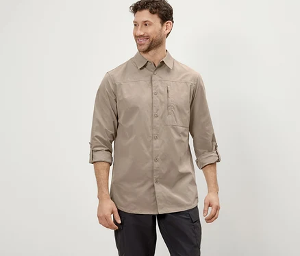 Ein Mann posiert in einem beigen Outdoorhemd mit Moskito-Schutz und einer schwarzen Hose.