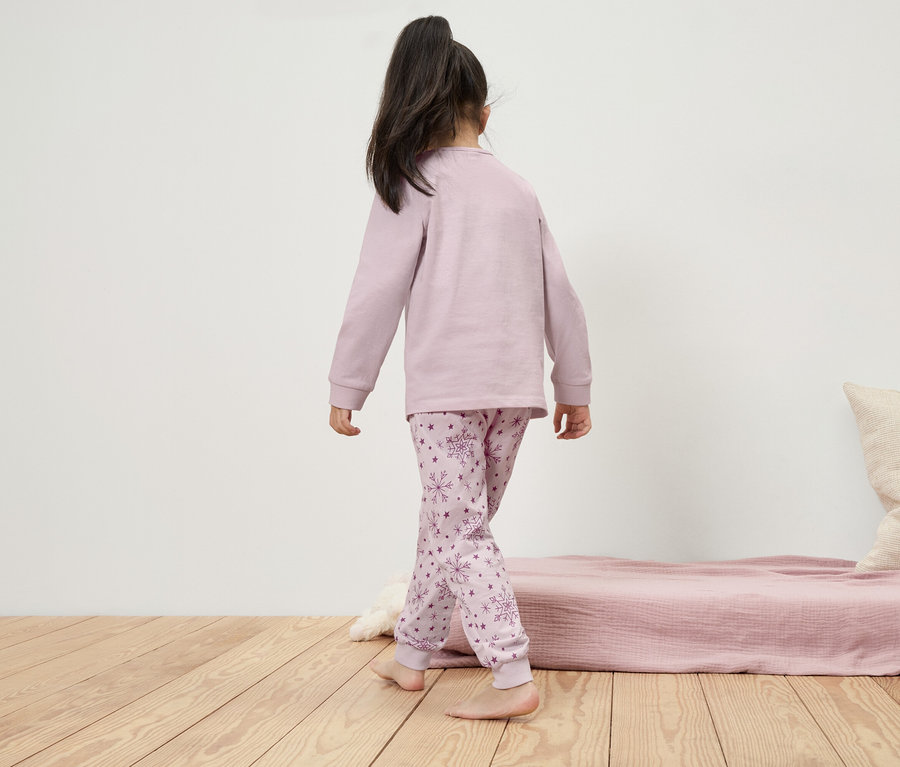 Mädchen im langärmeligen Pyjama mit Schneeflockenmuster geht über den Holzboden.