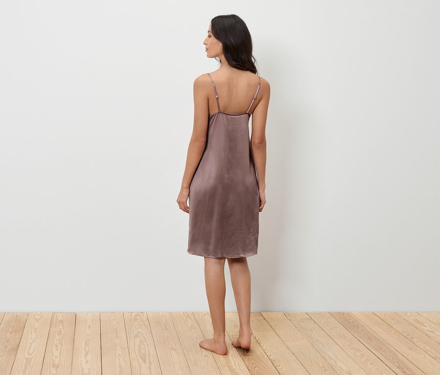 Frau steht mit dem Rücken zur Kamera und trägt ein violettes Nachthemd.