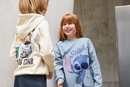 Zwei Kinder stehen vor einer Wand. Ein Kind trägt eine Kinder-Jogginghose und einen Hoodie mit Minecraft-Figuren. Das andere Kind trägt 3 Kinder-Leggings, schwarz, und ein Stitch-Shirt.