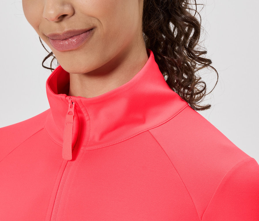 Nahaufnahme einer Frau mit lockigem Haar, die eine pinkfarbene Trainingsjacke mit Reißverschluss trägt.
