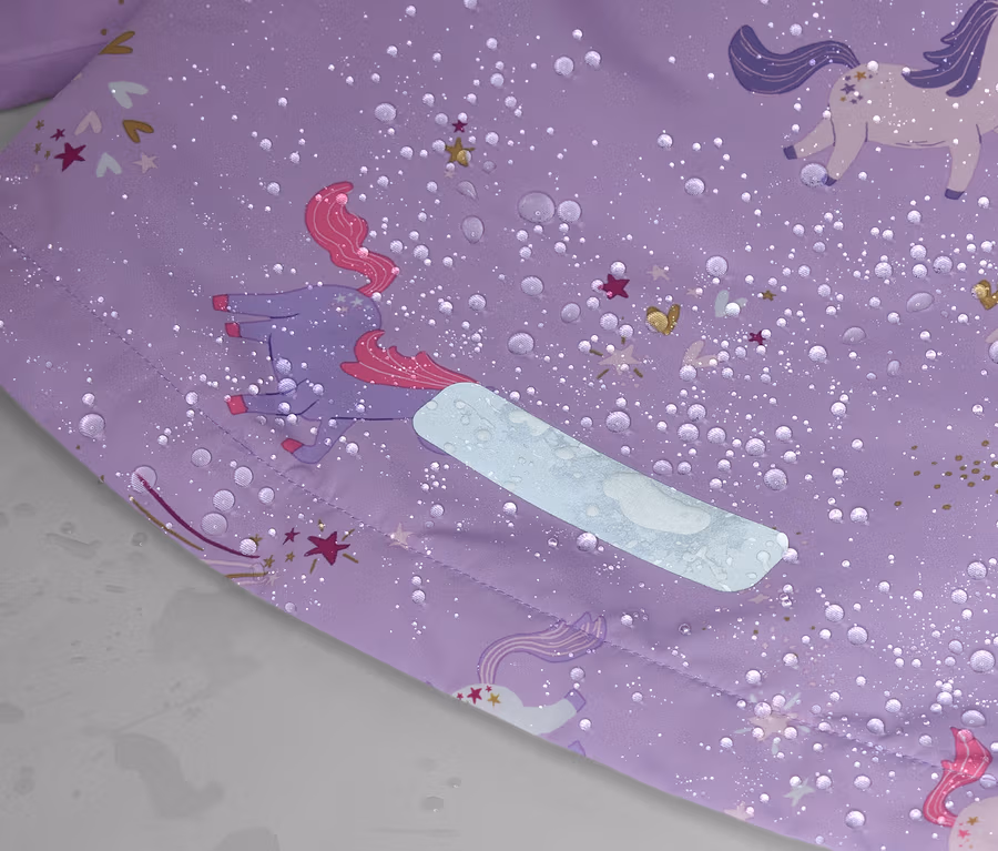 Nahaufnahme eines lila Stoffes mit Einhornmuster, Wassertropfen und einem reflektierenden Streifen.