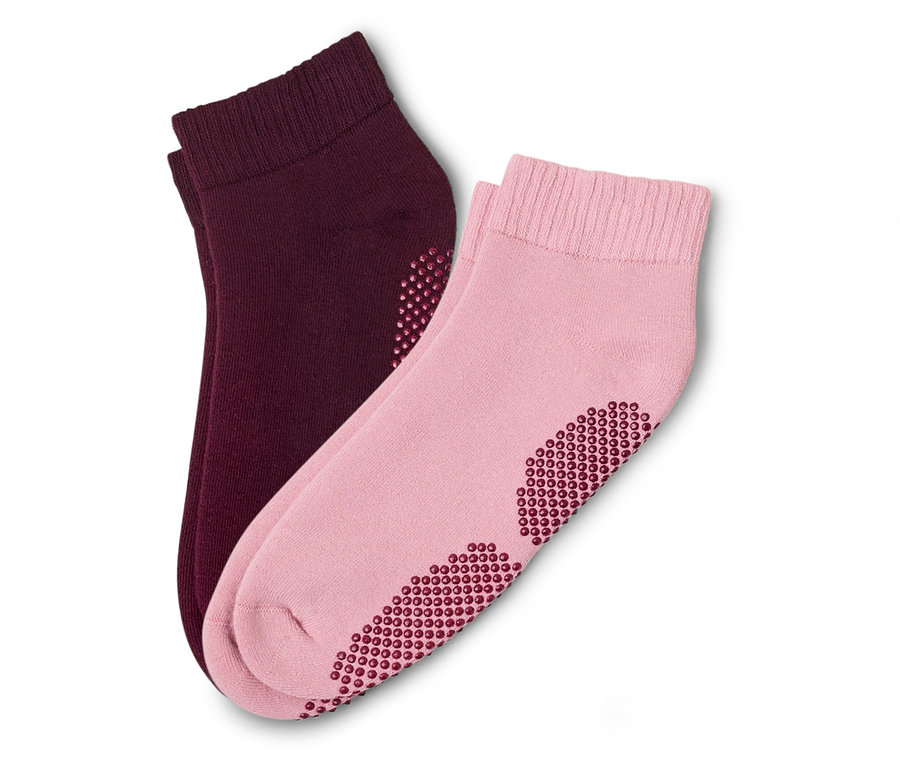 Ein Paar Socken, eine rosa und eine bordeauxrot, liegen übereinander. Beide haben Noppen an der Unterseite.