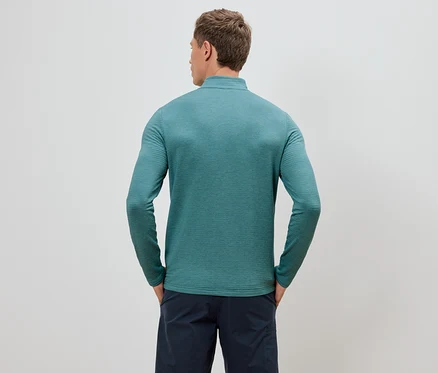 Mann von hinten in einem türkisfarbenen, langärmeligen Oberteil und marineblauen Shorts, die Hände in den Hosentaschen.