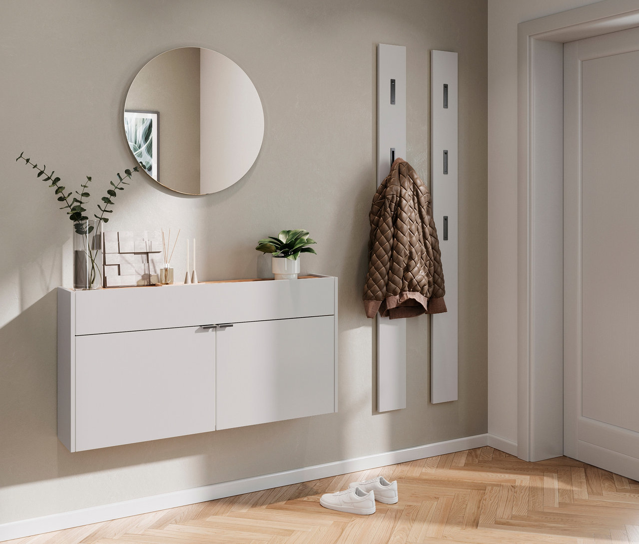 Flur mit weißem Hängeschrank unter rundem Spiegel, darüber Deko. Jacke hängt an weißer Garderobe neben Tür. Weiße Schuhe auf Parkett.